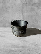 Vesseld.com Black textured bowl on a light gray surface with a concrete wall background